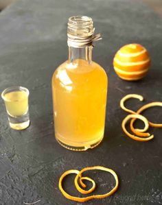 a bottle of liquid sitting on top of a table next to an orange and some glasses