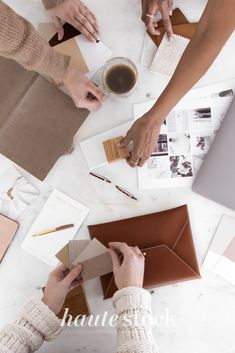 three people sitting at a table with envelopes and papers in front of them, one holding a cup of coffee