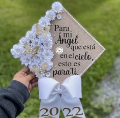 a person holding up a graduation cap with flowers on it in front of some grass