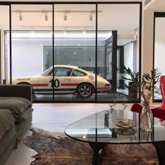 a living room filled with furniture and a car in the doorway to another room that has glass walls