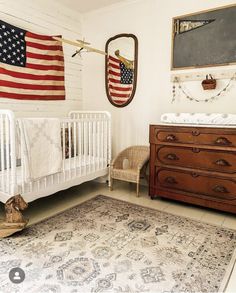 a baby's room with an american flag hanging over the crib and dresser