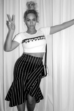 a black and white photo of a woman with her hands in the air, wearing a striped skirt