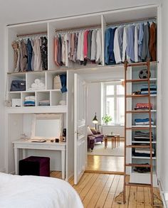 a bedroom with a bed, desk and shelves filled with clothes on top of them