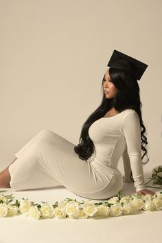 a woman sitting on the ground wearing a graduation cap and white dress with roses around her