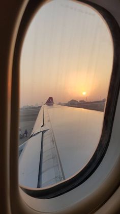 an airplane window with the sun setting in the distance as seen from it's wing