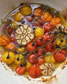 tomatoes, mushrooms and other vegetables are in a white bowl on the counter top with oil