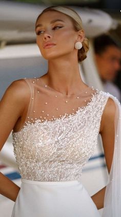 a woman in a white wedding dress standing next to a boat with her hands on her hips