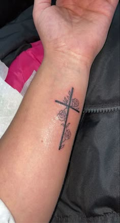 a woman's arm with a cross tattoo on it and flowers around the wrist