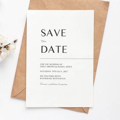 a white save the date card on top of a brown envelope next to some flowers