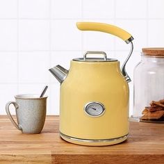 a yellow tea kettle sitting on top of a wooden table next to a mug and cookies