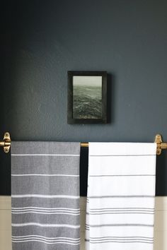 two towels are hanging on the towel rack in front of a black wall and framed photograph