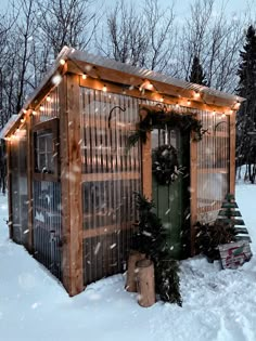 a small wooden building with lights on it in the snow near some trees and bushes