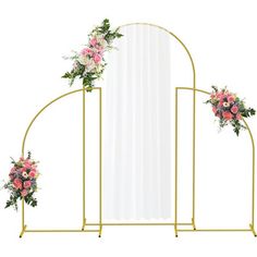 a white and gold arch with pink flowers on it, next to a wall mirror