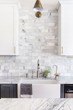 a kitchen with marble counter tops and white cabinets, gold faucet light over the sink