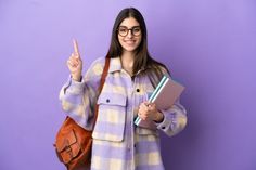 a young woman holding a book giving the peace sign while standing against a purple wall