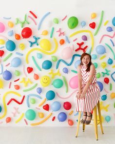 a woman standing in front of a wall covered with balloons and confetti on it