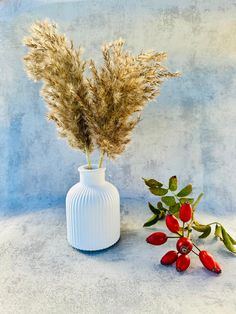 a white vase filled with flowers next to a red berry plant on a blue background