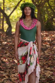 a woman in a green top and floral skirt with pink beads on her head standing in leaves