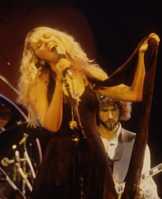 a woman singing into a microphone while standing next to a man with a guitar on stage