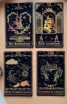 four tarot cards with gold foil designs on them, sitting on a wooden surface