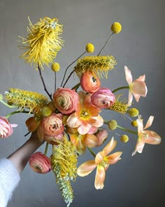 a person holding a bouquet of flowers in their hand, with yellow and pink colors