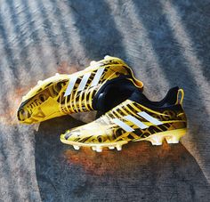 a pair of yellow and white adidas soccer shoes on the ground with shadows coming from behind them