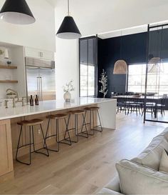 an open kitchen and living room area with bar stools in the foreground, dining table on the far side