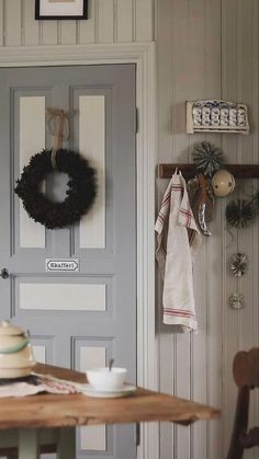 a table and chair in front of a door with a wreath hanging on the wall