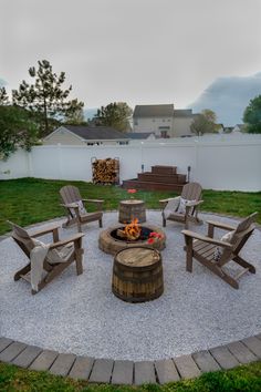 a fire pit surrounded by wooden chairs in the middle of a yard with gravel around it