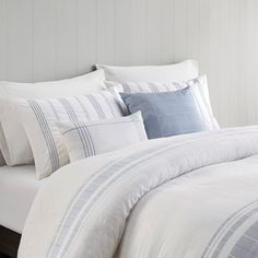 a white bed with blue and grey striped comforter set on it's side