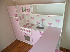 a toy kitchen with pink and white decor on the walls, stove top oven and sink