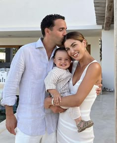 a man, woman and child standing in front of a house smiling at the camera