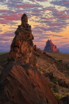 a rock formation in the middle of a field with mountains in the background at sunset