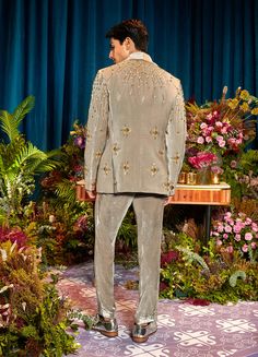 a man in a suit standing on a stage with flowers and greenery behind him