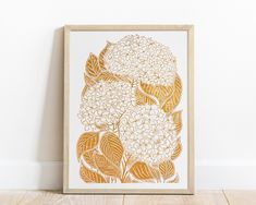 an art print with flowers in gold and white on a wooden floor next to a wall