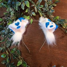 two white and blue feathered hair clips on top of green leaves next to a wooden table