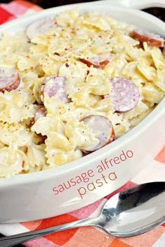 a white bowl filled with pasta and sausage on top of a checkered table cloth