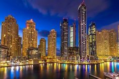 the city skyline is lit up at night with boats in the water and tall buildings