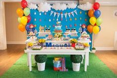 a table topped with lots of cake next to a blue wall covered in balloons and streamers