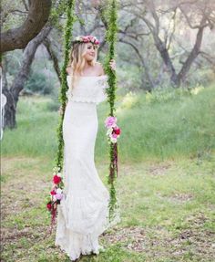 a woman in a white dress is standing on a swing with flowers and greenery