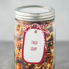 a jar filled with taco soup sitting on top of a counter next to a red and white tag