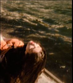 a woman laying on top of a boat in the water with her eyes closed and head down