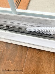 a white brush sitting on top of a window sill next to a wooden floor