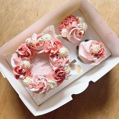 two cupcakes with pink frosting and white flowers in a box on a table