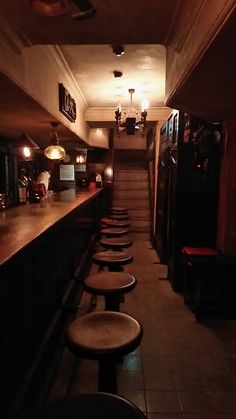 a dimly lit bar with stools in the foreground and stairs leading up to it