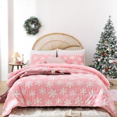 a bed with pink and white comforter next to a christmas tree