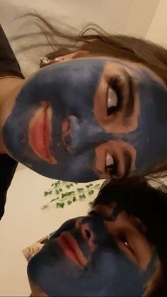 two people with their faces covered in blue clay and green leaves, one is looking at the camera