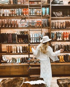 a woman standing in front of a store filled with lots of boots and hats on display