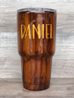 a wooden tumbler with the word daniel written on it and gold lettering in yellow