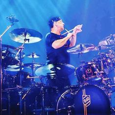 a man playing drums on stage with blue lighting behind him and his hands in the air